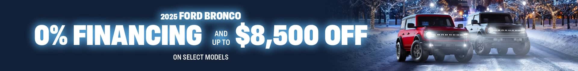 Two 2025 Ford Broncos, one red and one silver, sit on a snowy winter road with glowing city lights and decorated trees behind them. Large text highlights zero percent financing OAC and up to eighty five hundred dollars off select models.