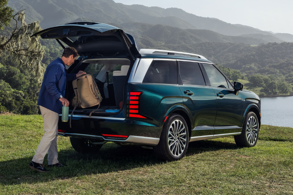 Rear three-quarter view of a green Hyundai Palisade with the tailgate open as a person loads gear outdoors