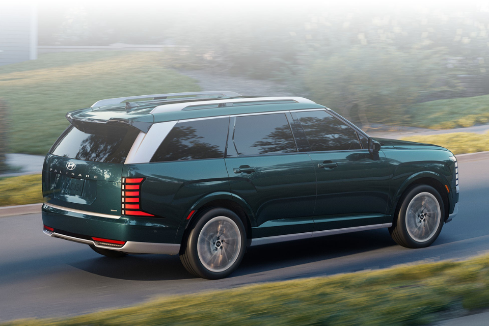 Rear three-quarter driving view of a green Hyundai Palisade on a suburban road