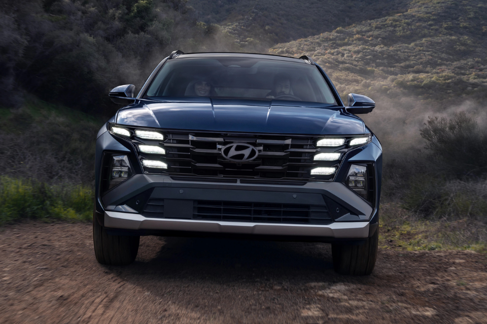 Front fascia of the 2026 Hyundai Tucson Hybrid illuminated at dusk, emphasizing its bold grille and LED signature.