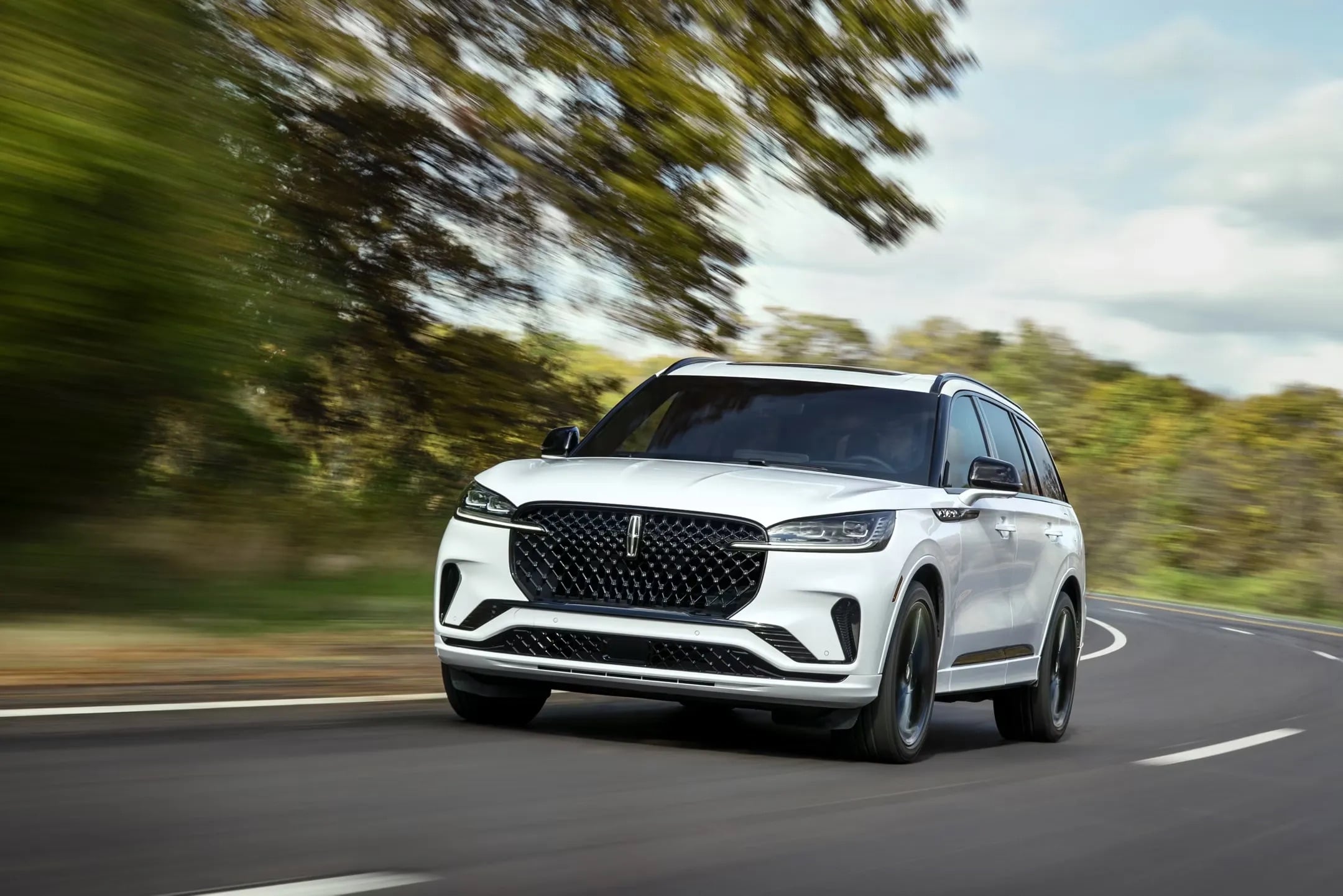 2026 Lincoln Aviator white luxury SUV driving on scenic tree lined road