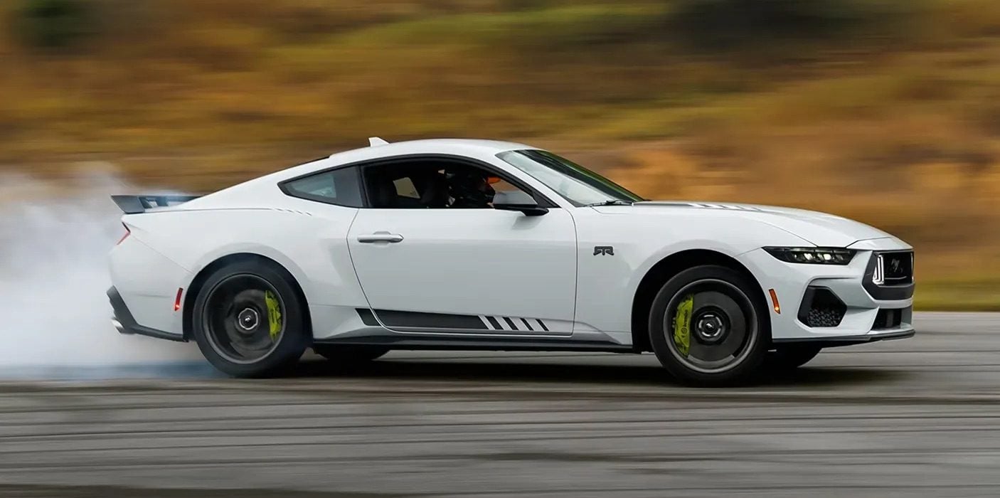 "2026 Ford Mustang in white performing a high-speed drift on a track with smoke trailing from the rear tires, showcasing its performance and handling capabilities."