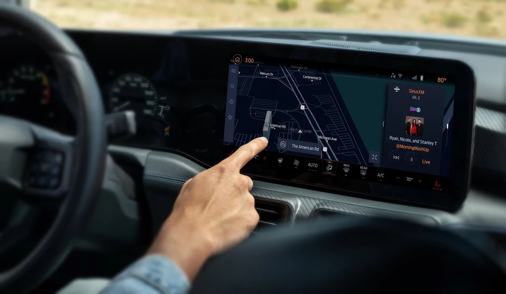 A person using a touchscreen infotainment system inside a 2026 Ford Mustang. The screen displays a navigation map. The dashboard and steering wheel are partially visible, and the climate controls are shown below the screen.