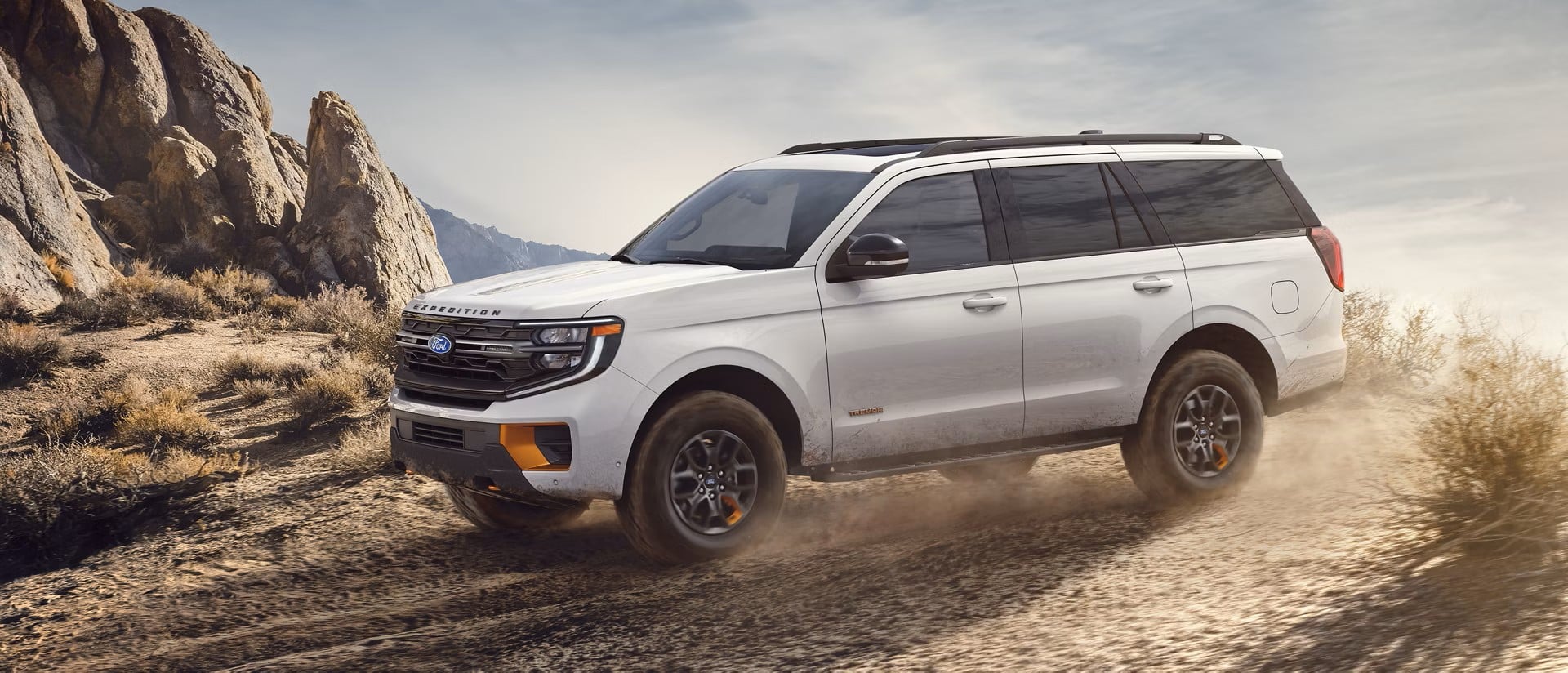 White 2027 Ford Expedition driving on a coastal road beside rocky cliffs