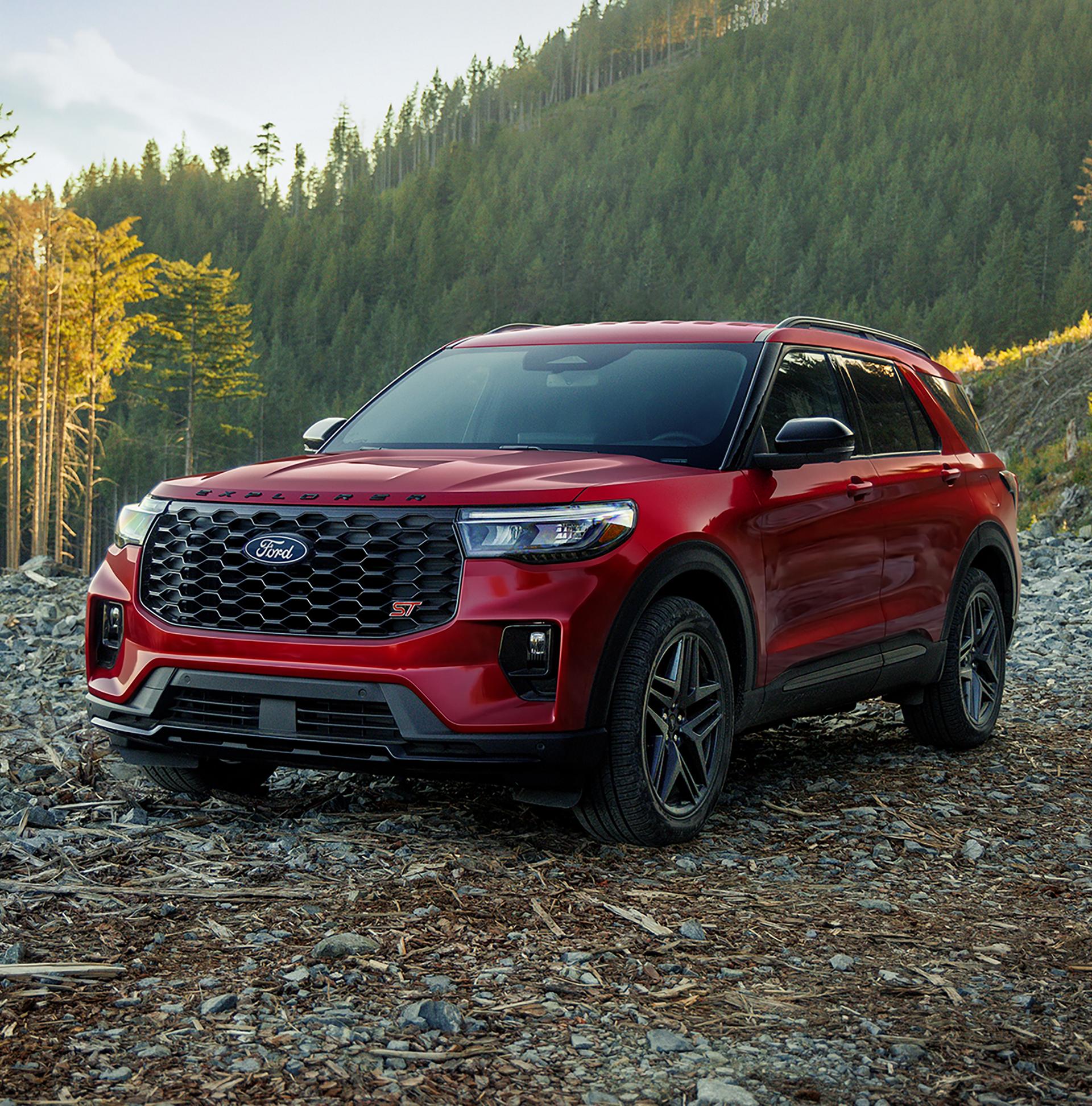 Red Ford Explorer parked on rocky ground beside a forest