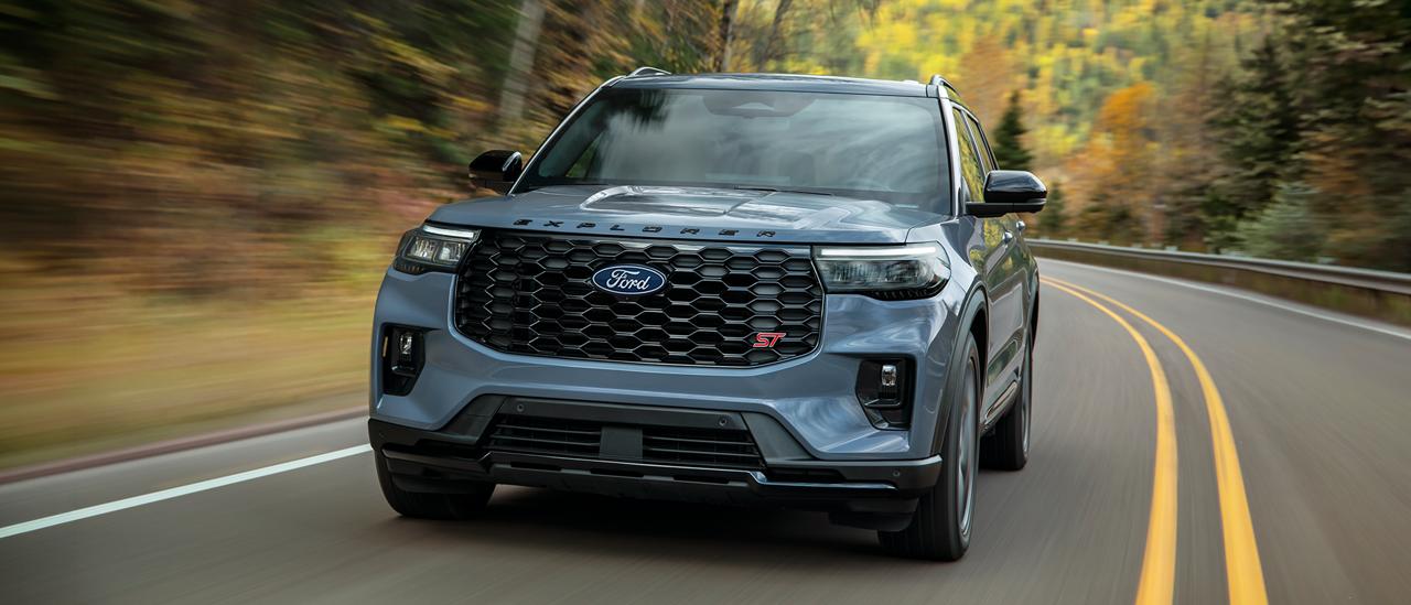 Grey Ford Explorer driving along a winding road through autumn trees