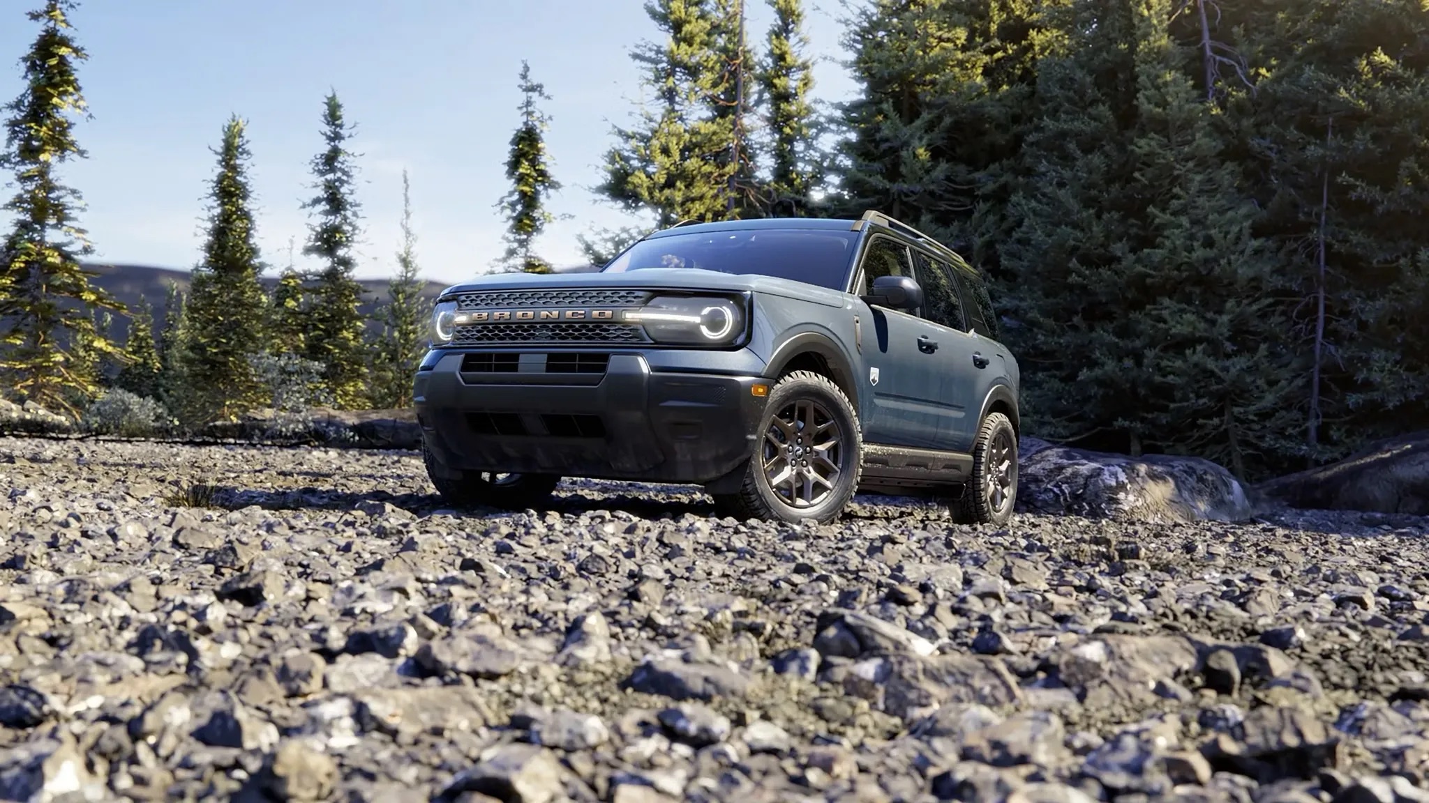 2026 Ford Bronco Sport driving across a gravel road surrounded by trees