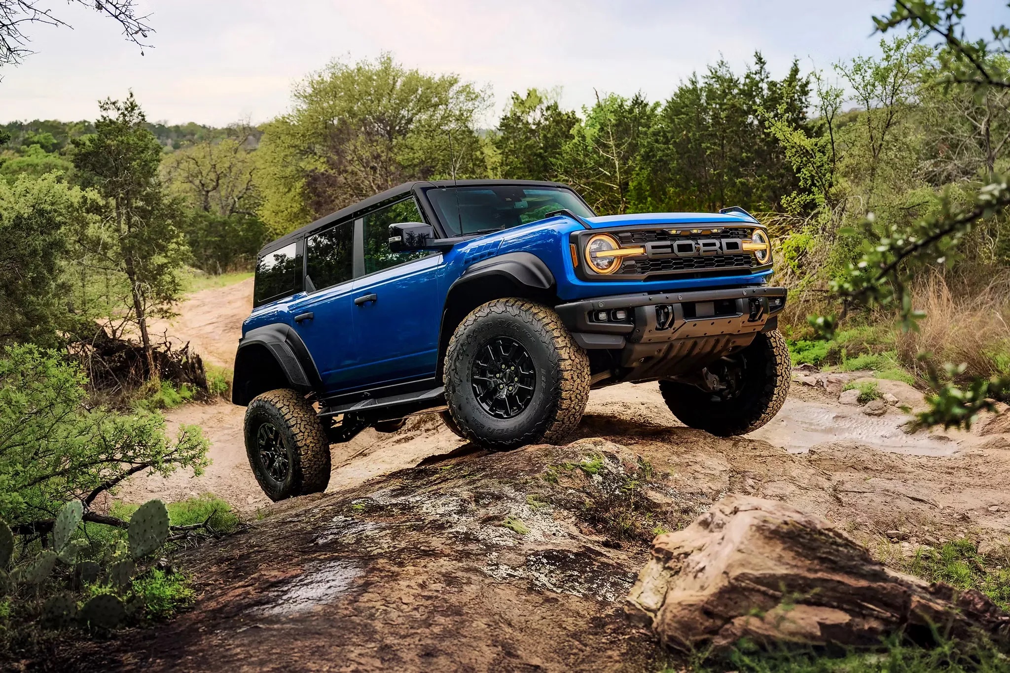 Ford Bronco navigating a rugged off-road trail, kicking up dirt and showcasing its suspension, all-terrain tires, and 4x4 capability.