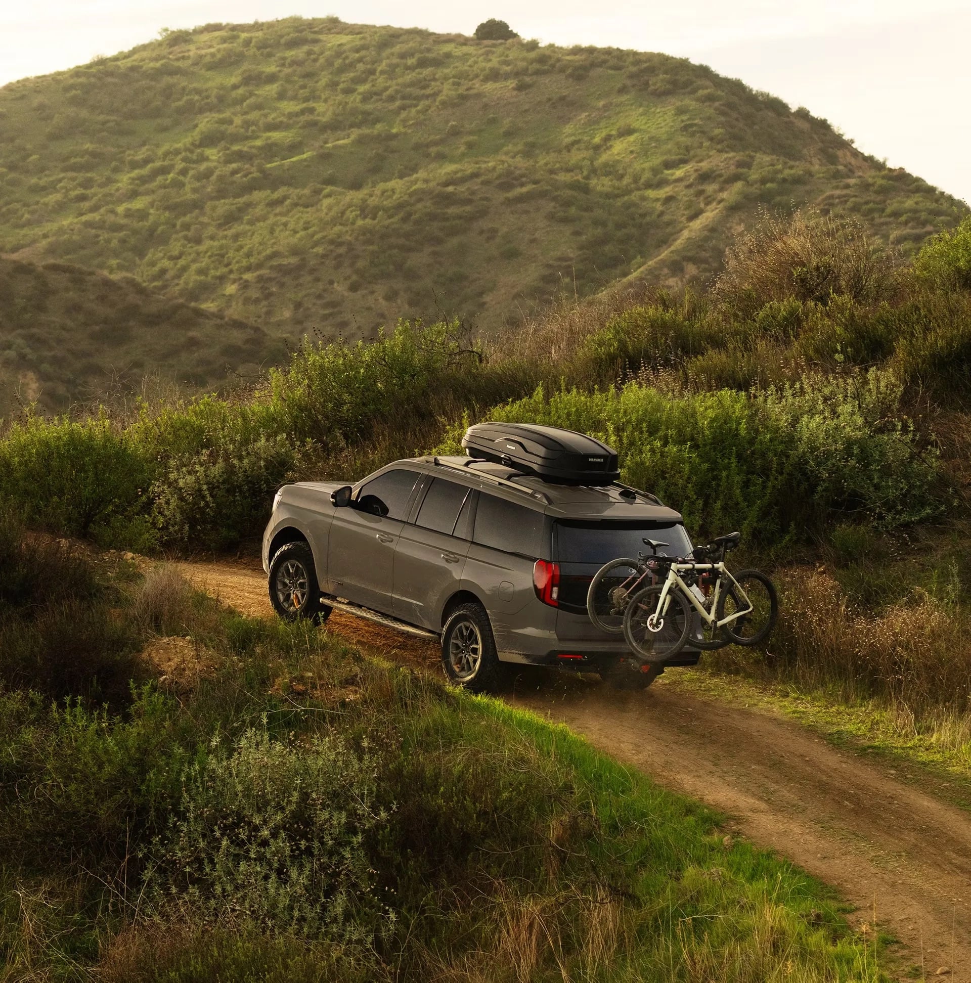 Ford Expedition towing a bicycle trailer through rolling hills at sunset.