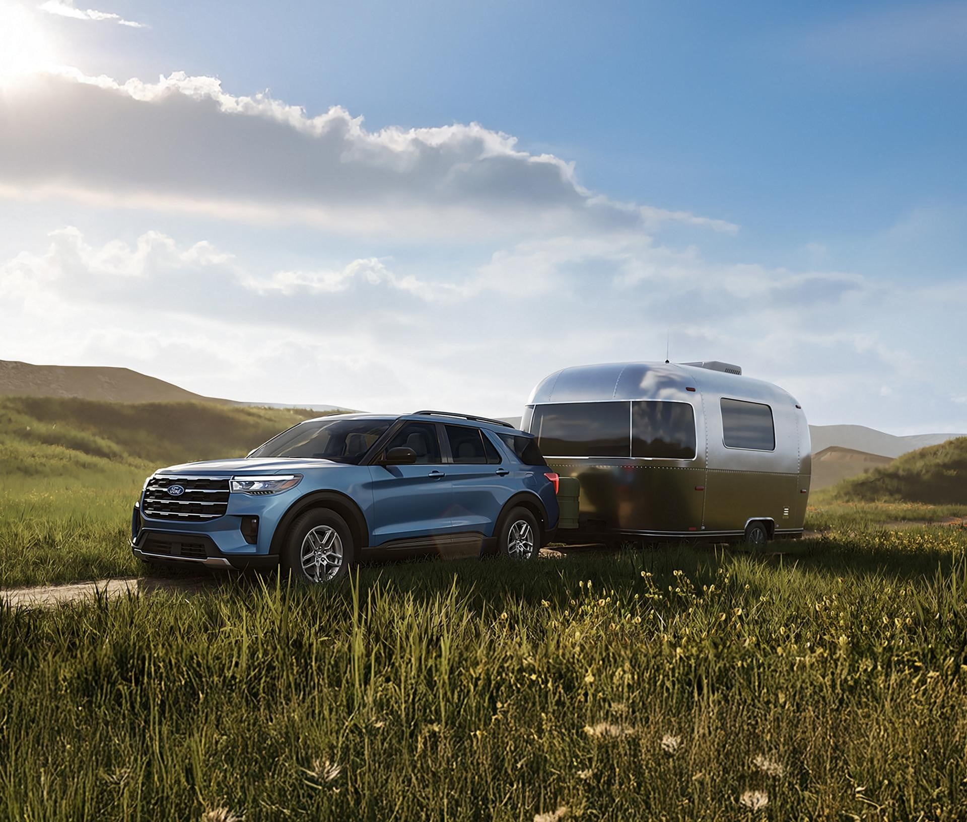 2027 Ford Explorer towing a travel trailer through an open grassy landscape