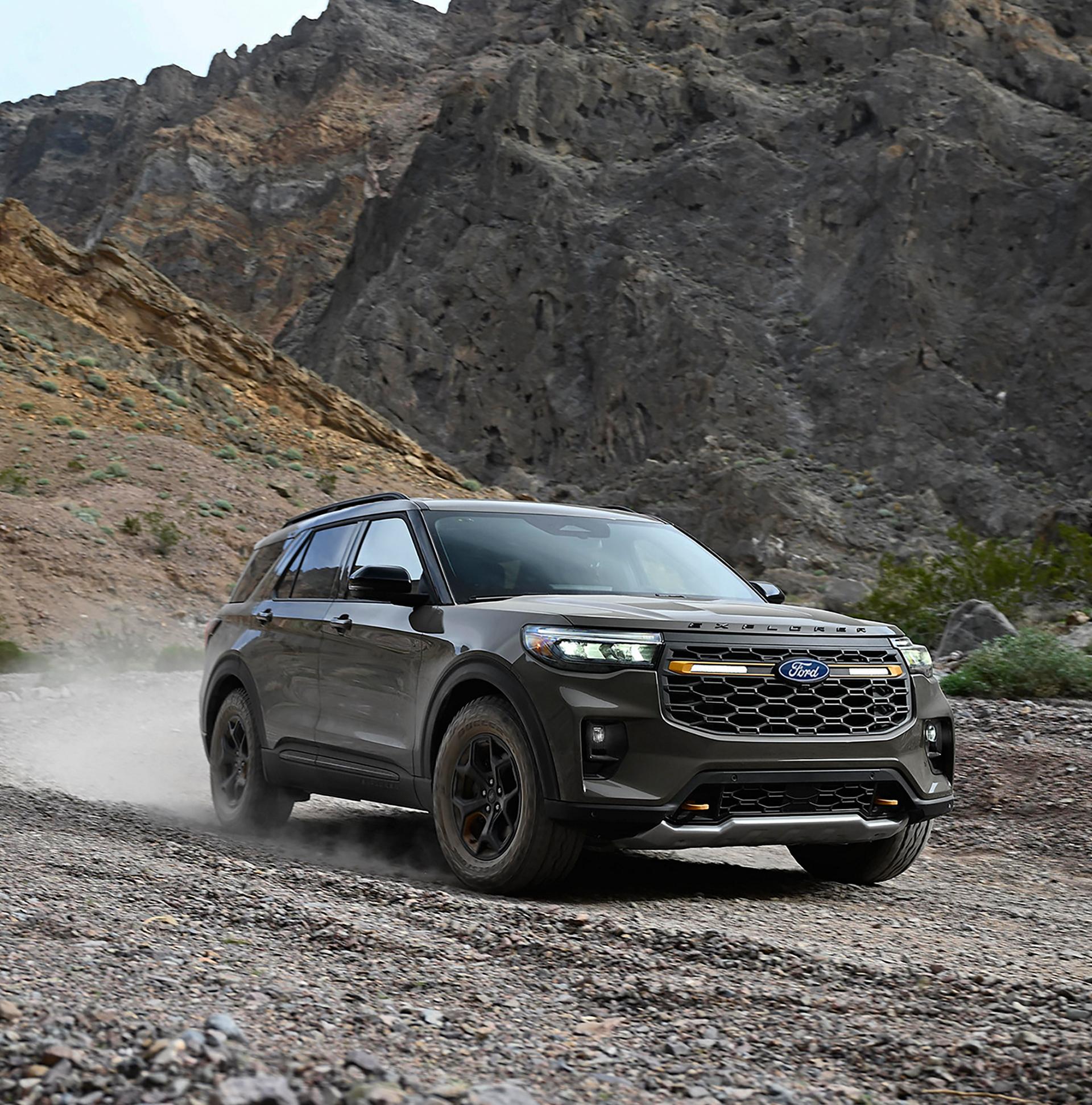 2027 Ford Explorer driving on a dusty gravel road beside rocky hills