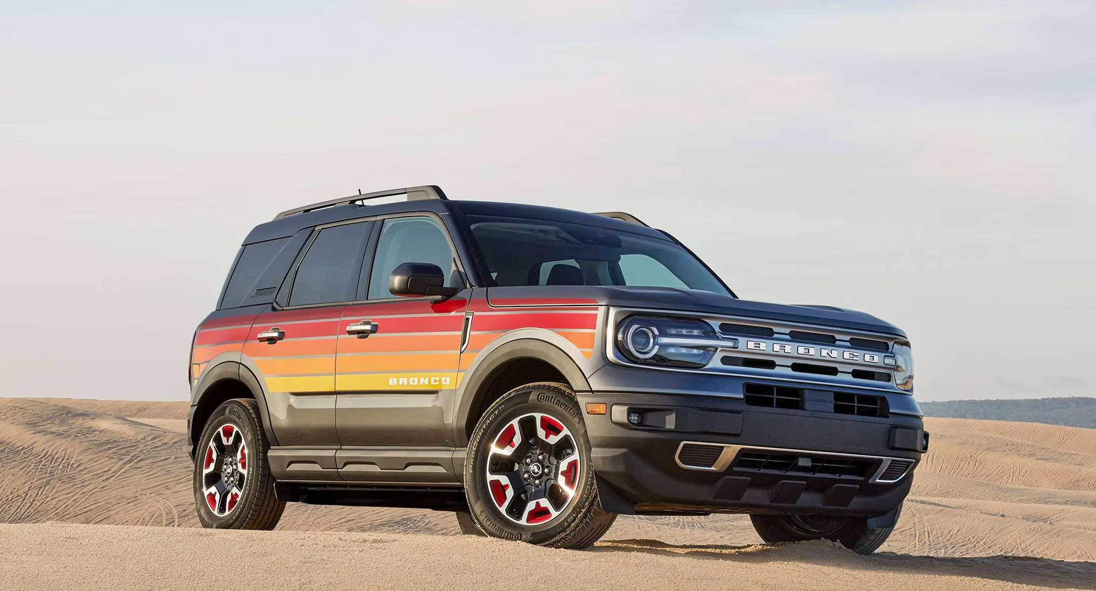 A special-edition Ford Bronco Sport Free Wheeling Edition in a desert setting, featuring retro sunset-inspired graphics and red-accented wheels. The image captures a mix of modern capability and vintage-inspired style.