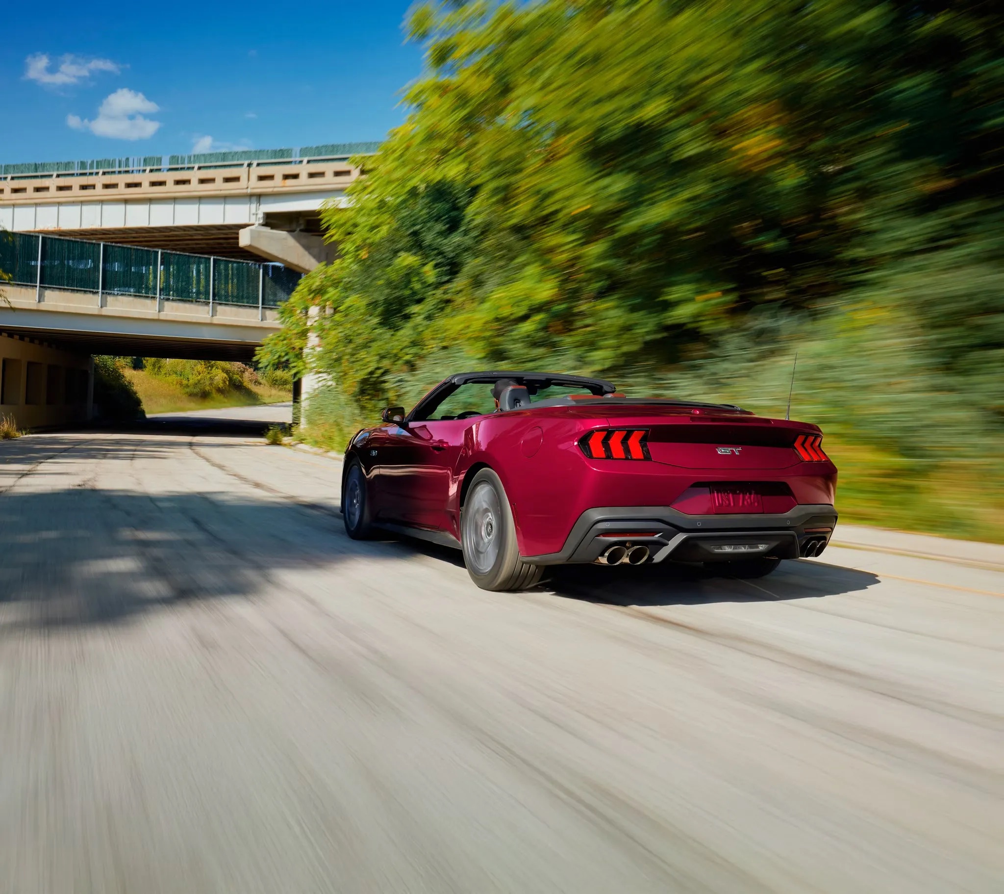 2026 Ford Mustang red sports car driving rear view on road