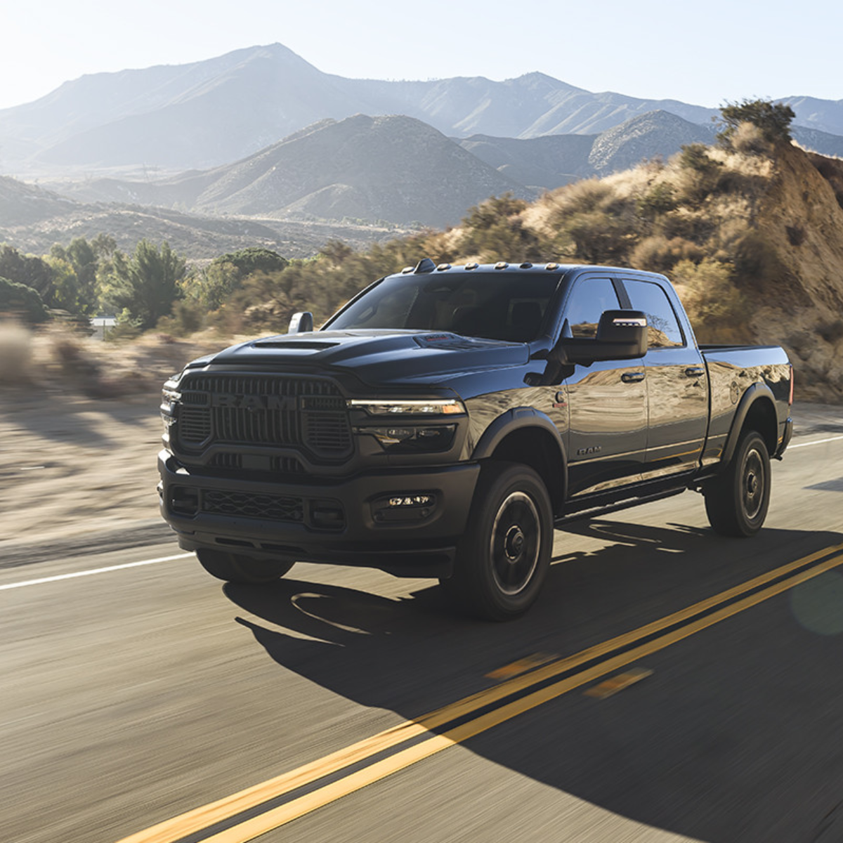 Black 2025 Ram 2500 HD driving on a desert highway with mountains in the background