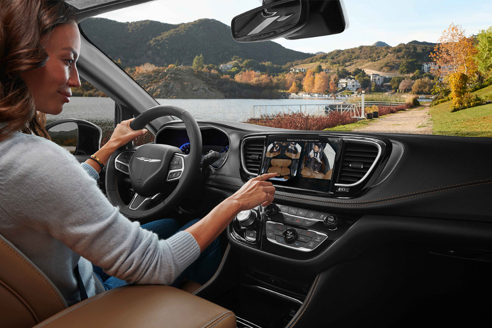 Interior view of the 2026 Chrysler Pacifica with driver using the touchscreen display while parked near a lake.