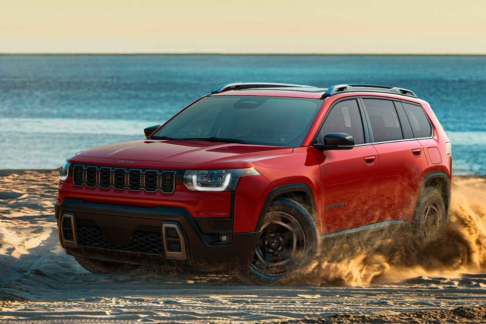 2026 Jeep Cherokee in red driving across sandy beach terrain near the water, emphasizing rugged performance and versatility