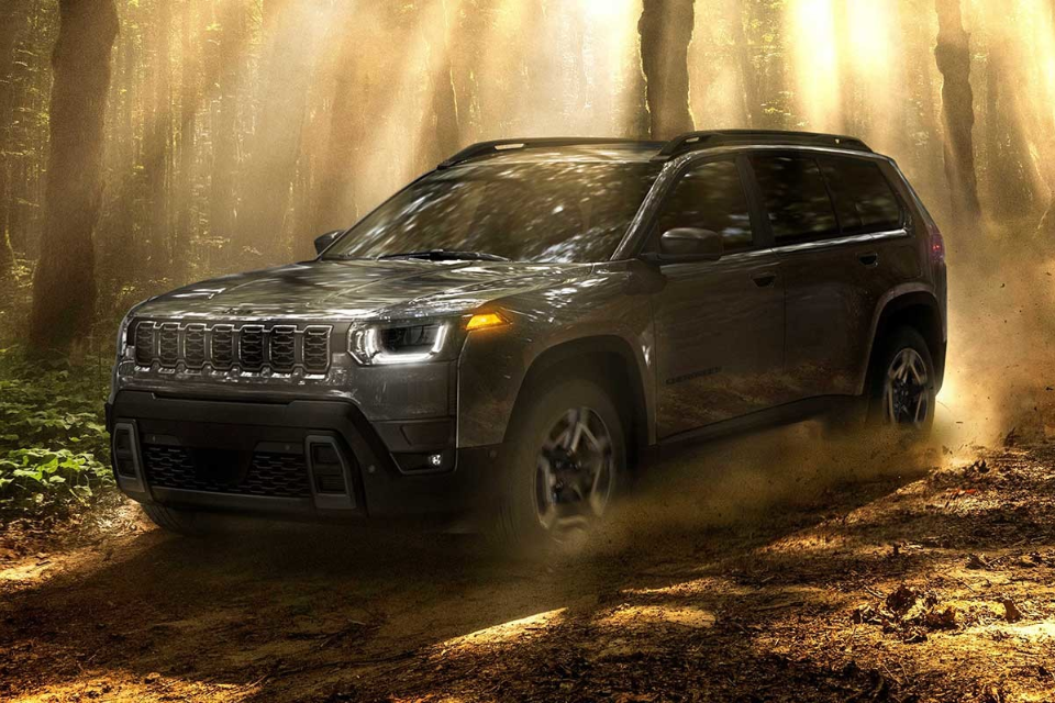 2026 Jeep Cherokee in black driving through a forest trail with sunlight streaming through the trees, showcasing off-road capability