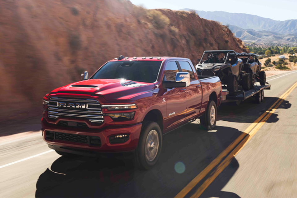 2026 Ram 2500 HD in red towing two ATVs on a trailer through a desert highway, showcasing powerful towing capability