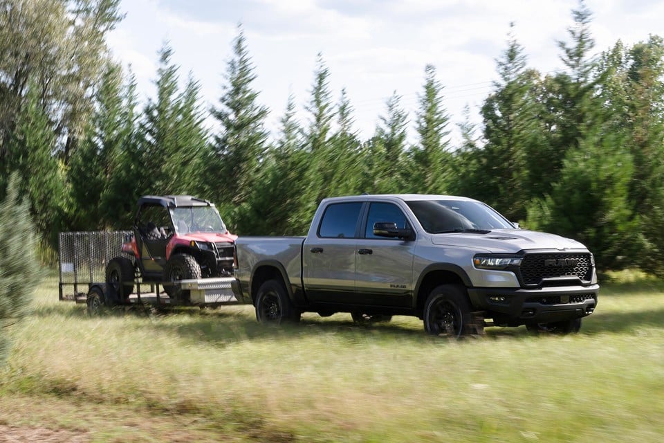 2026 Ram 1500 towing an off-road ATV on a trailer through a grassy field, emphasizing powerful towing capability
