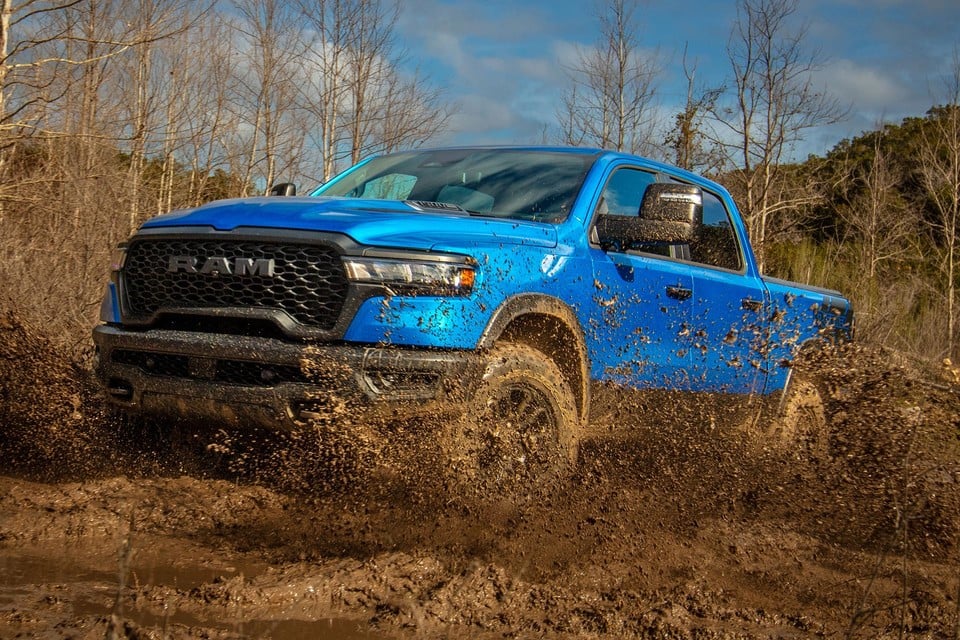 2026 Ram 1500 in blue driving through deep mud, showcasing its rugged off-road capability and durable exterior design