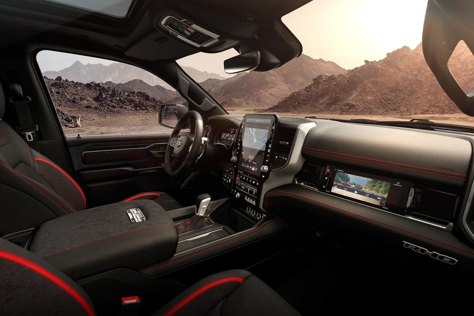Front cabin of the 2026 Ram 1500 highlighting a digital touchscreen display, red-accented seats, and rugged modern design
