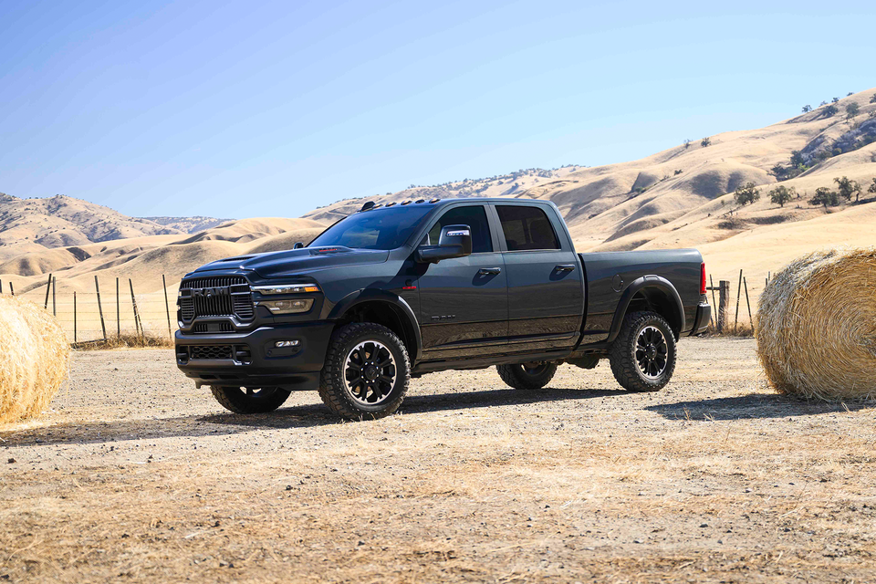 2026 Ram 2500 HD in black parked in an open rural field surrounded by hay bales, showcasing rugged design and high ground clearance