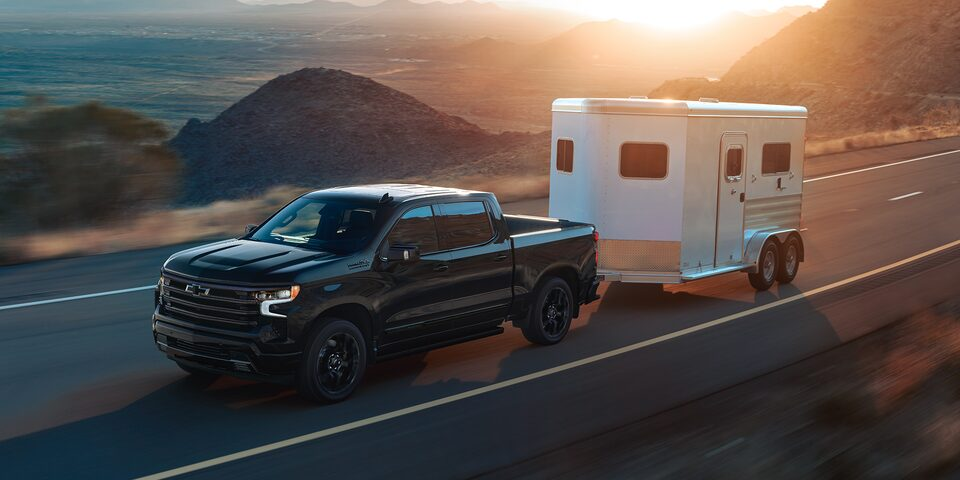 A 2025 Chevrolet Silverado LD towing a trailer while driving alone on the road.
