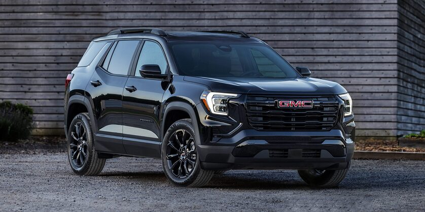 Front-side view of the 2025 GMC Terrain parked beside a wooden structure on a gloomy day