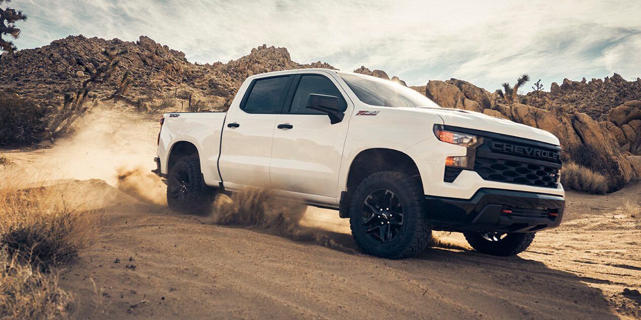 Three quarters view of a white 2025 Chevrolet Silverado LD under a sunny day on a desert.