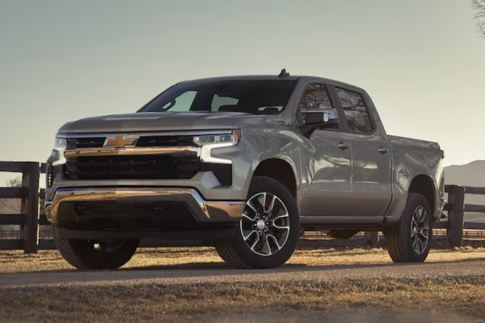2026 Chevrolet Silverado 1500 in silver parked on a country road at sunset, showcasing its bold design and strong stance