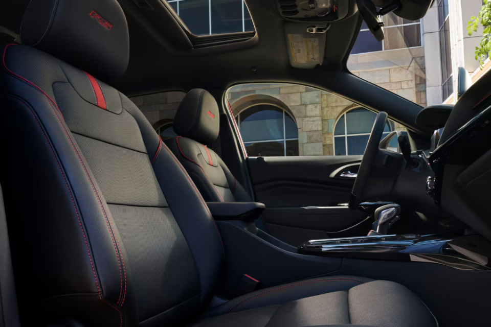 Front seat interior of the 2026 Chevrolet Trax RS with red stitching, sport-style seats, and a panoramic sunroof