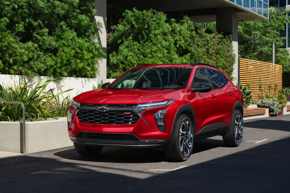 Front three-quarter view of a red 2026 Chevrolet Trax parked in an urban setting, highlighting its bold styling