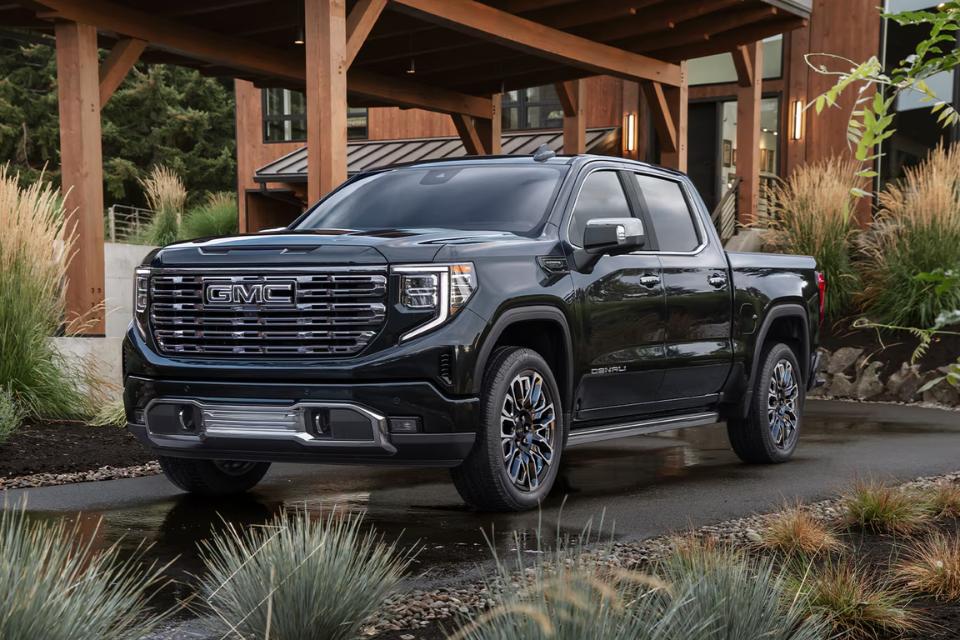 Front view of the 2026 GMC Sierra 1500 Denali parked in front of a modern home, highlighting its upscale design and chrome detailing