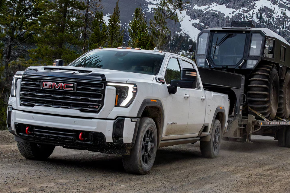 2026 GMC Sierra HD AT4 towing heavy equipment through a mountain road, demonstrating impressive towing capability