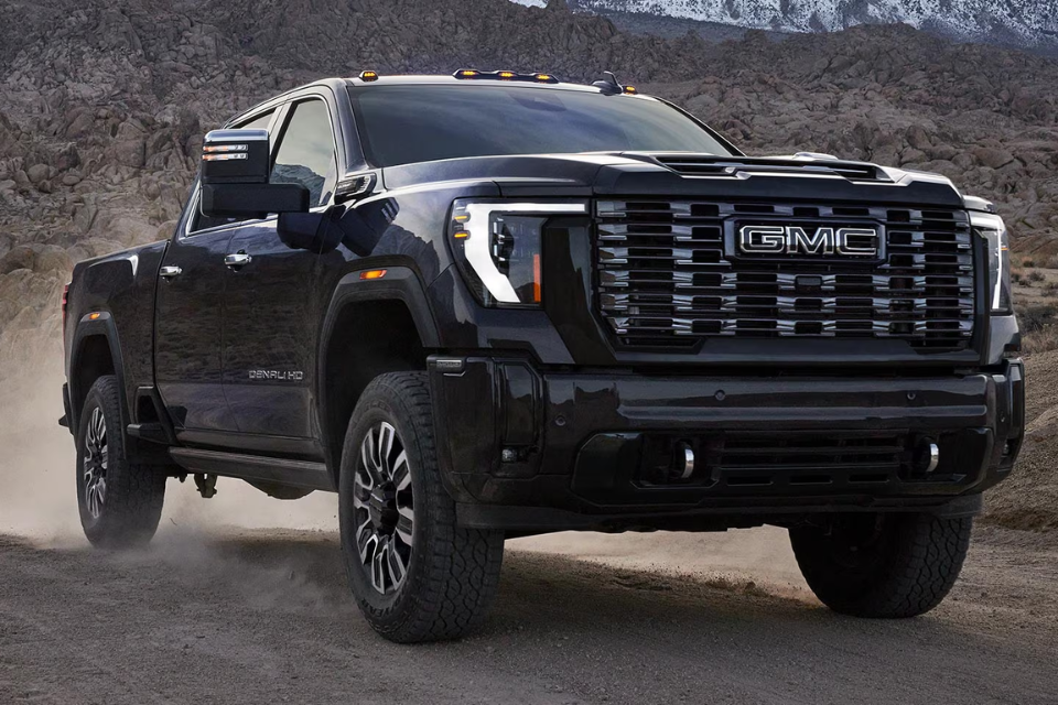 2026 GMC Sierra HD Denali driving through rugged terrain, emphasizing its power and premium exterior styling