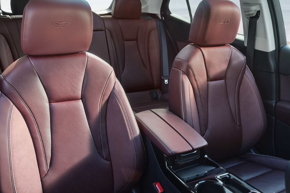 Front seats of a red Buick Envision ST showing perforated leather upholstery with ST logos and a centre console