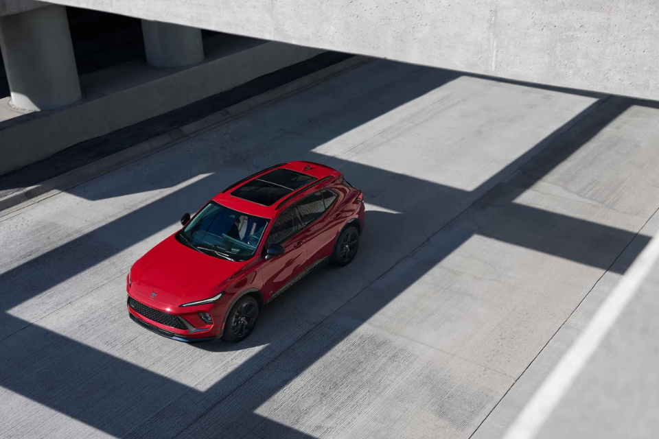 Overhead view of a red Buick Envision driving beneath a modern concrete overpass with dramatic light and shadow patterns