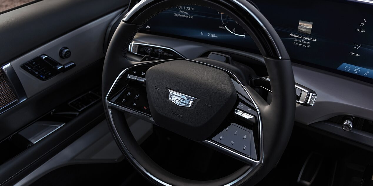 Steering wheel with Cadillac crest, touch-sensitive controls, and a panoramic curved LED display in the background.
