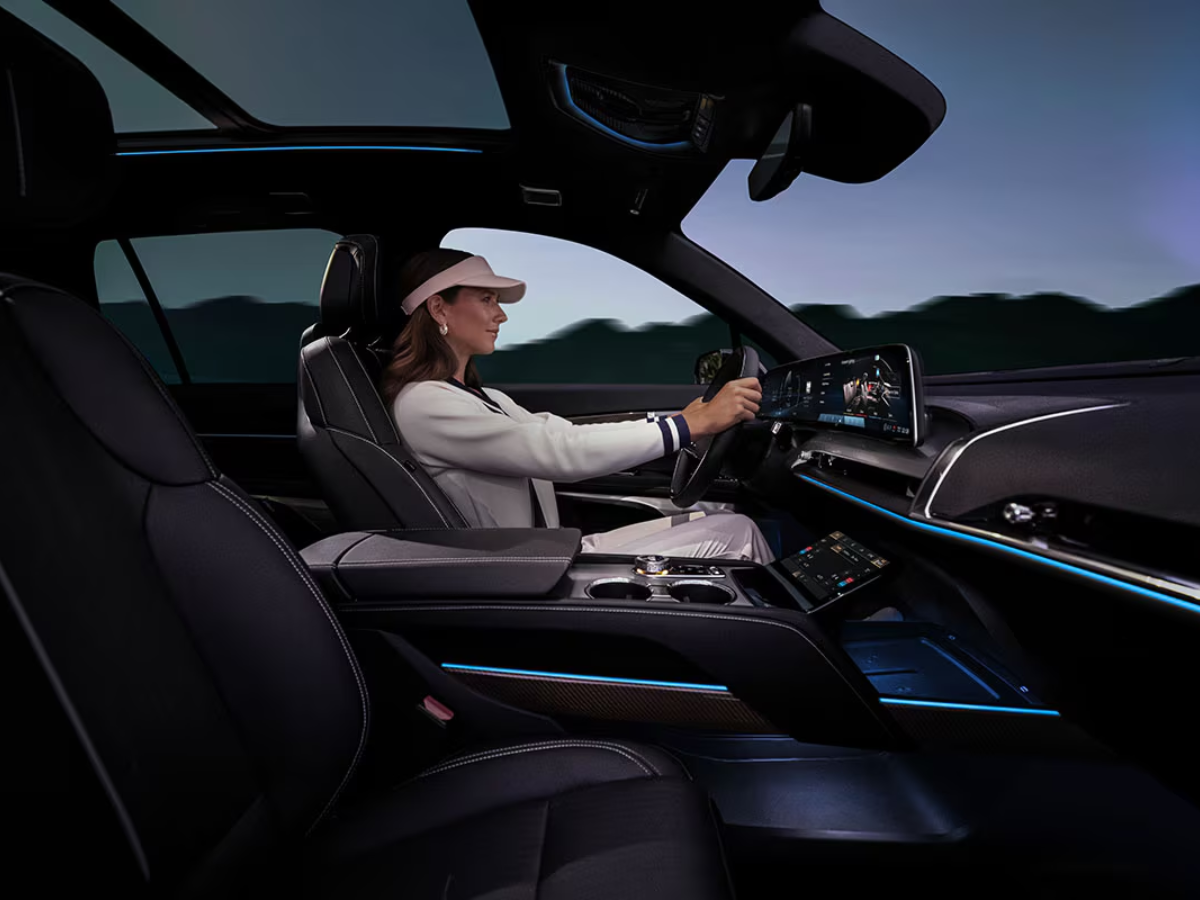 Woman driving the 2026 Cadillac VISTIQ with illuminated interior ambient lighting and panoramic curved dashboard display