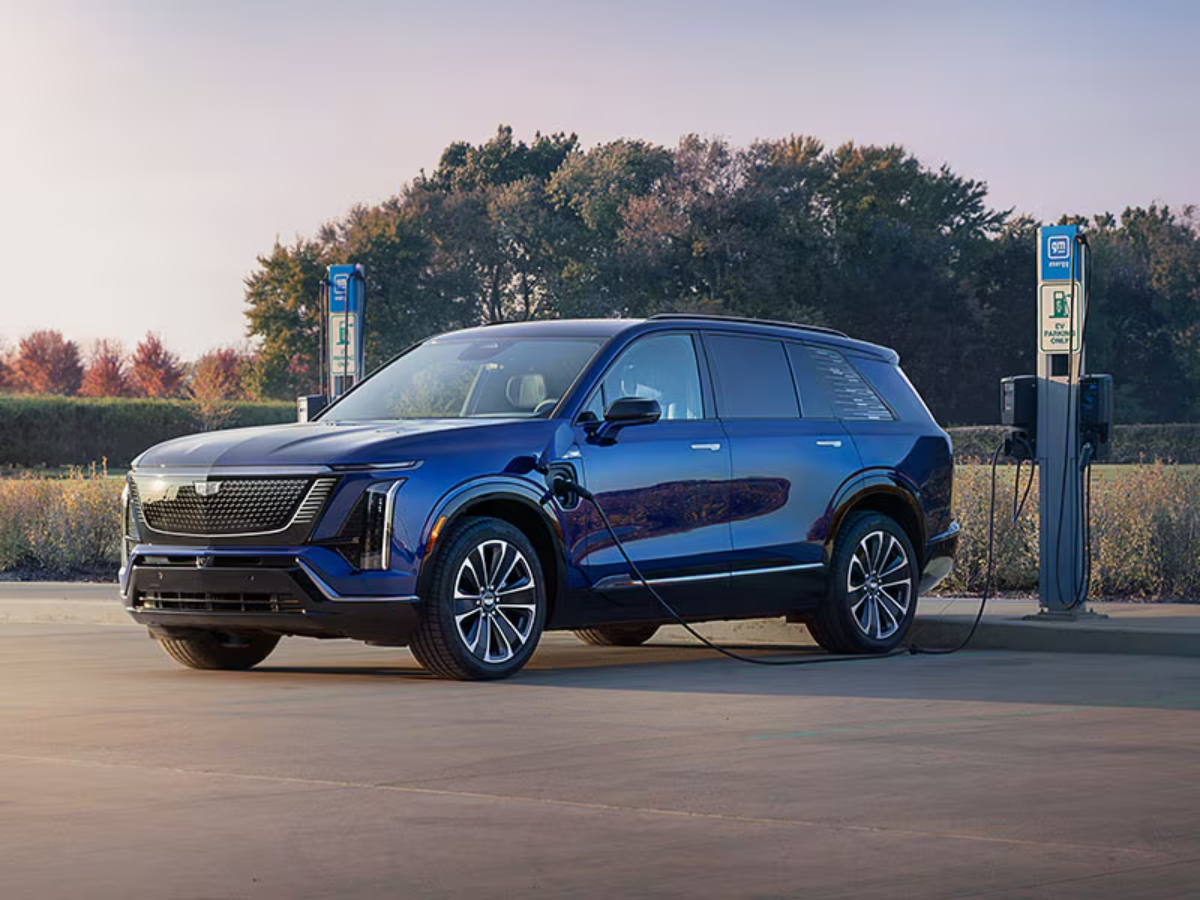 2026 Cadillac VISTIQ connected to a GM Energy charging point in an outdoor lot with trees in the background