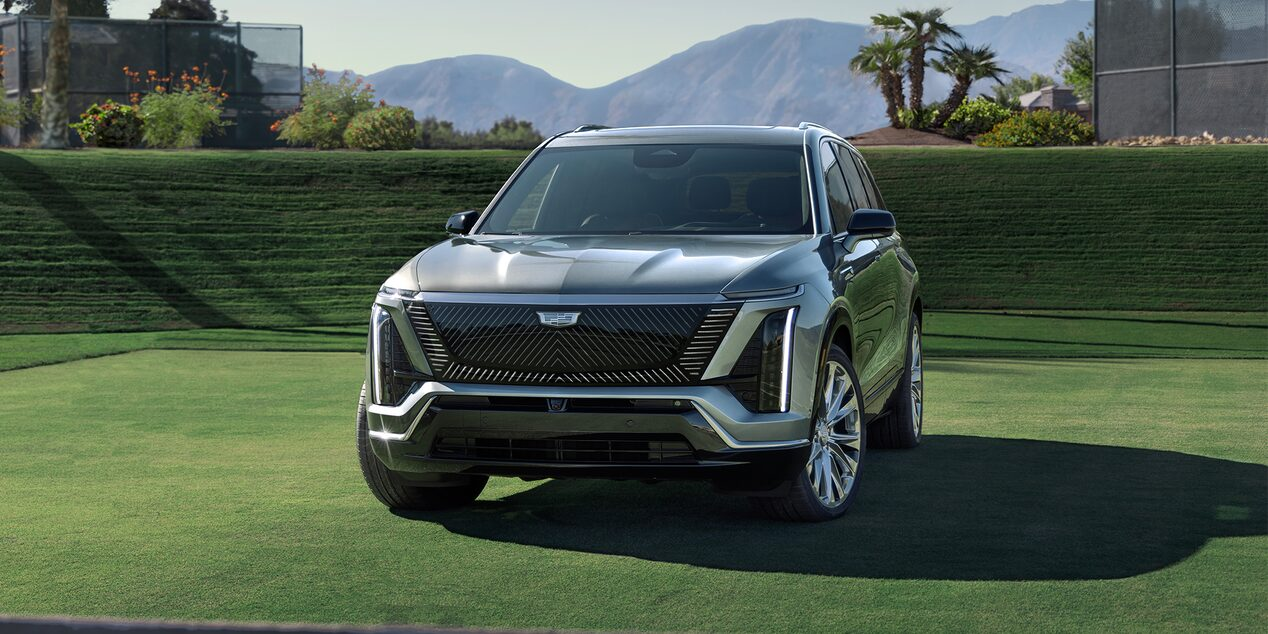 Parked on green grass with mountain backdrop, showcasing vertical LED headlights and bold grille design