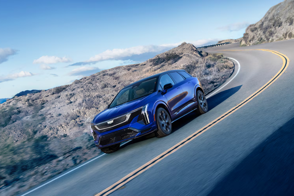 Blue 2026 Cadillac Optiq navigating a winding mountain road, highlighting its precise handling and aerodynamic profile
