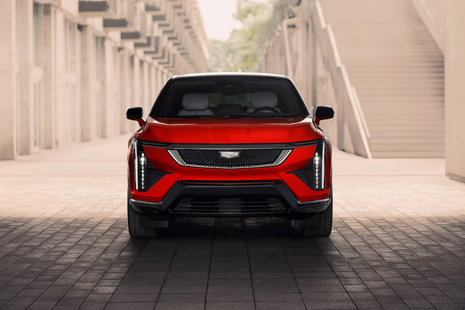 Front view of the 2026 Cadillac Optiq highlighting its bold grille and vertical LED headlights in a contemporary urban setting