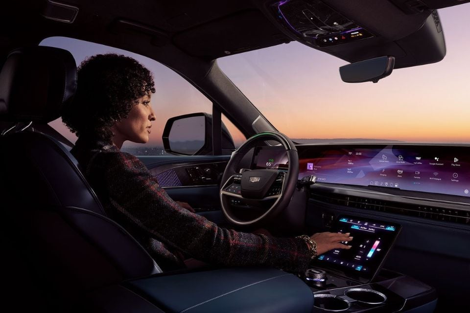 Driver using the touchscreen interface inside the 2026 Cadillac Escalade IQ at sunset