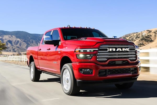 Red 2025 Ram 2500 HD driving on a sunny rural road with mountains in the background