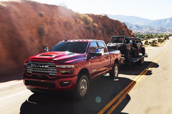 Red 2025 Ram 2500 HD towing a trailer with off-road vehicles along a desert highway