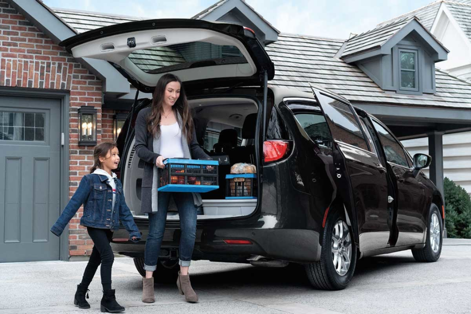 Mother and daughter unloading groceries from the 2026 Chrysler Grand Caravan parked in a suburban driveway