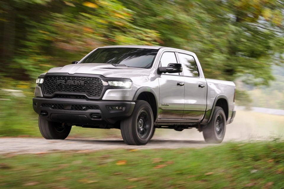 2026 Ram 1500 in silver driving down a country road surrounded by trees, emphasizing its confident handling